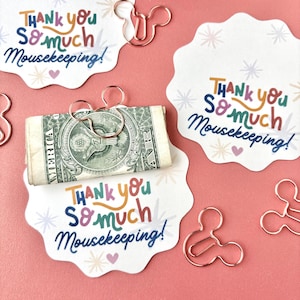 May include: White scalloped cards with the text Thank you so much Mousekeeping! in colorful letters, accompanied by rose gold metal paper clips shaped like mouse heads. One card holds a rolled-up one-dollar bill secured by a mouse-shaped clip.