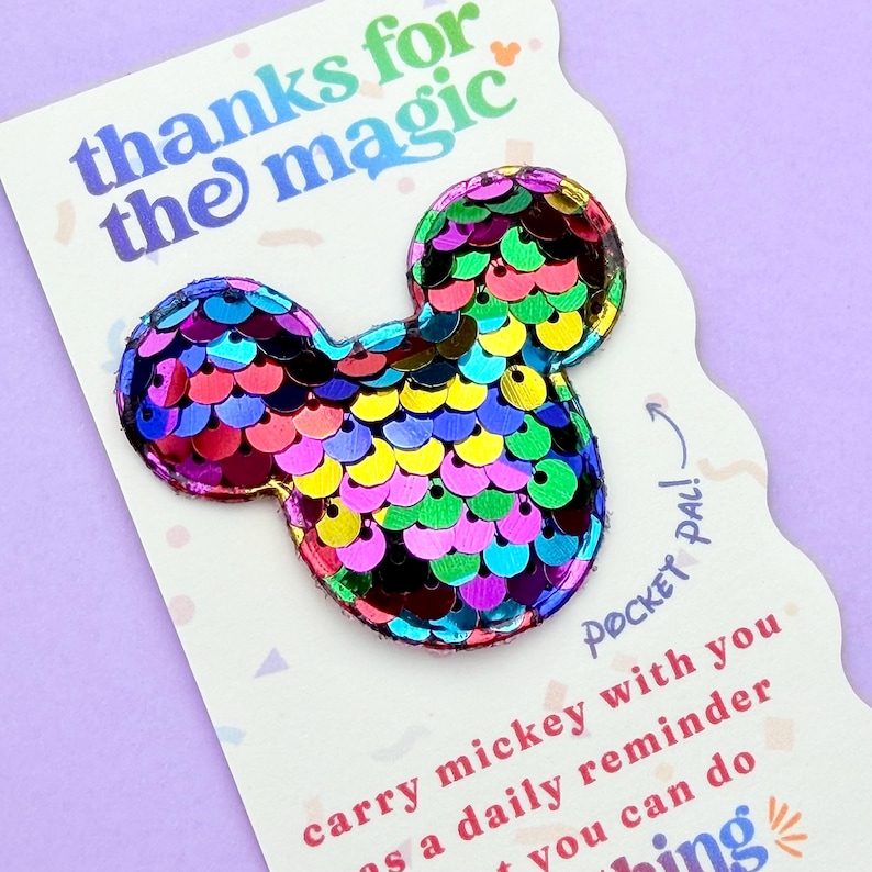 A close-up view of a rainbow sequin Mickey mouse shape attached to a white card that reads thanks for the magic.