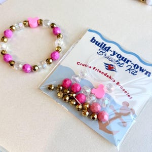 A pink beaded friendship bracelet with a central pink Mickey head charm lies next to an unopened DIY kit.