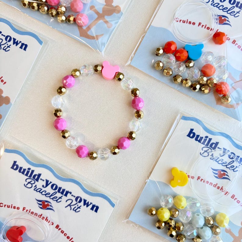 Four packaged bracelet kits with different color themes are arranged with a completed pink beaded bracelet in the center.