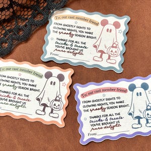 May include: Three rectangular scalloped-edge cards with Halloween themes. Each card features a ghost with mouse ears holding a pumpkin bucket and text that reads: To: our cast member friend, From ghostly sights to glowing nights, you make the spooky season bright. Thanks for all the tricks & treats you've brought us pure delight. From:.