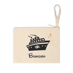 May include: Cream-colored zippered pouch featuring a black illustration of a cruise ship with Mickey Mouse ears. The name "Brandon" is written in a script font below the ship. Two gold stars are to the right of the ship.