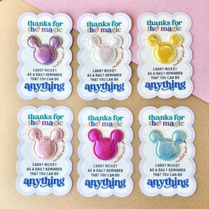 May include: Six wallet-sized Mickey Mouse-shaped patches in various colors: purple, white, yellow, pink, fuchsia, and blue. Each patch is on a white card with text that reads "thanks for the magic" and "carry Mickey as a daily reminder that you can do anything."