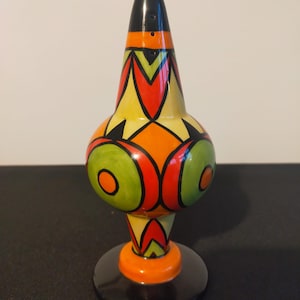 May include: A hand-painted ceramic salt shaker with a black top and base. The body is yellow with orange, red, and green geometric patterns. The salt shaker is approximately 15 cm tall.