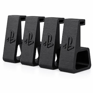 May include: Four black, L-shaped controller stands arranged in a row. Each stand features a textured surface and a raised PlayStation logo on the front face. The design includes a top hook and a wide, stable base for holding gaming controllers.