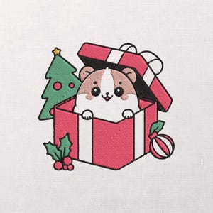 Puede incluir: Diseño bordado con un hámster asomando por una caja de regalo roja. Un árbol de Navidad verde, un adorno rojo y blanco y acebo completan la escena festiva. El diseño está sobre un fondo blanco.