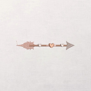 Puede incluir: Diseño de flecha en oro rosa bordado sobre tela blanca. La flecha tiene un emplumado en forma de hoja y una punta de flecha. El eje presenta tres corazones pequeños y uno más grande en el centro.