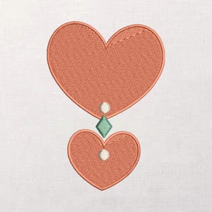 Puede incluir: Diseño bordado con dos corazones color coral, uno grande y otro pequeño, conectados por un diamante verde y círculos blancos. Los corazones tienen una apariencia texturizada, sobre un fondo blanco.