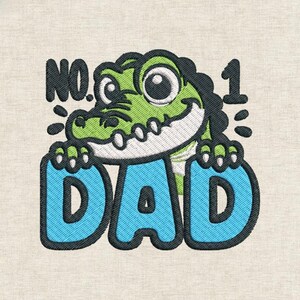 Könnte beinhalten: Gesticktes Design mit einem lächelnden grünen Alligator mit großen Augen. Der Alligator hält das Wort "DAD" in blauen Buchstaben. Über dem Alligator steht der Text "NO. 1". Das Design befindet sich auf einem beigen Stoff.