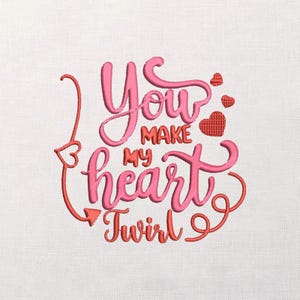 May include: Embroidered design on white fabric. The text reads "You Make My Heart Twirl" in pink script, with red accents including hearts and an arrow. A romantic, Valentine's Day theme.
