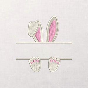 Puede incluir: Diseño bordado con orejas de conejo blancas con interior rosa sobre una línea horizontal, y dos patas de conejo con almohadillas rosas debajo de una segunda línea horizontal. El diseño está sobre un fondo blanco.