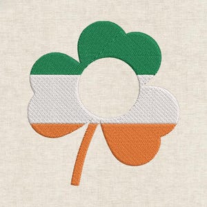May include: Embroidered shamrock design in green, white, and orange, resembling the Irish flag. The shamrock has a circular opening in the center and a stem. The design is on a beige fabric background.