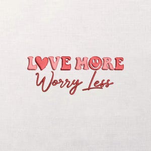May include: Embroidered text on a white background reads "LOVE MORE Worry Less." The word "LOVE" is in a gradient pink, with a heart replacing the "O." The word "MORE" has a smiley face replacing the "O." The text is in a cursive font.