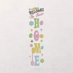 May include: Embroidered vertical sign with the words "WELCOME To Our HOME" in pastel colors. The design includes Easter-themed elements like eggs, flowers, and a carrot. The sign is on a white background.