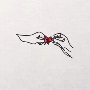 May include: An embroidered design of two hands holding a red heart with a pink outline. The hands are outlined in black thread, and the heart has a textured appearance. The background is a plain white fabric.