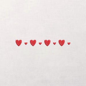 Può includere: Tessuto bianco con una fila di cuori rossi ricamati. I cuori variano in dimensioni, con cuori più grandi alternati a quelli più piccoli. Il ricamo ha un aspetto strutturato, aggiungendo profondità al design.