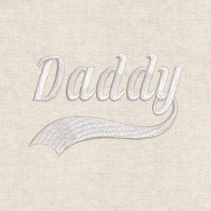 May include: Embroidered text reading "Daddy" in a script font with a decorative tail. The text and tail are in a light grey colour, stitched onto a beige fabric background. The design is simple and elegant.