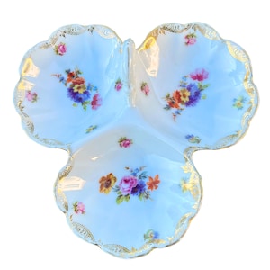 Peut inclure: Un plat de service en porcelaine blanche avec trois sections, chacune décorée d'un motif floral dans des tons de rose, jaune et bleu. Le plat est bordé d'une garniture dorée.