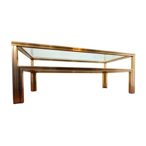 Peut inclure: Table basse rectangulaire avec un plateau en verre transparent et une étagère inférieure. Le cadre est en métal doré. La table a un design simple et géométrique et convient à un salon.