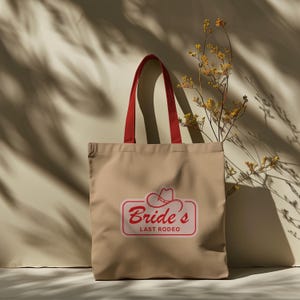May include: Beige tote bag with red handles and a red and white logo that says "Bride's Last Rodeo" with a cowboy hat graphic.