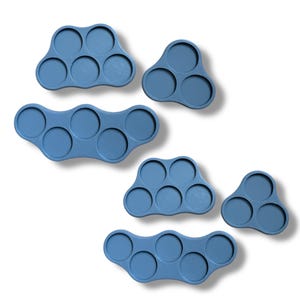 May include: Set of five blue plastic trays with circular indentations for holding small objects. The trays are in various shapes, including a cloud, a triangle, and a wavy shape.