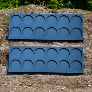 May include: Two blue plastic trays with 12 circular depressions each. The trays are designed to hold small round objects, such as paint pots or other craft supplies.