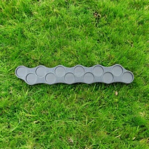 May include: A gray, plastic drink holder with ten circular indentations. The holder is designed to hold multiple cups or glasses. The object is placed on a bed of green grass.