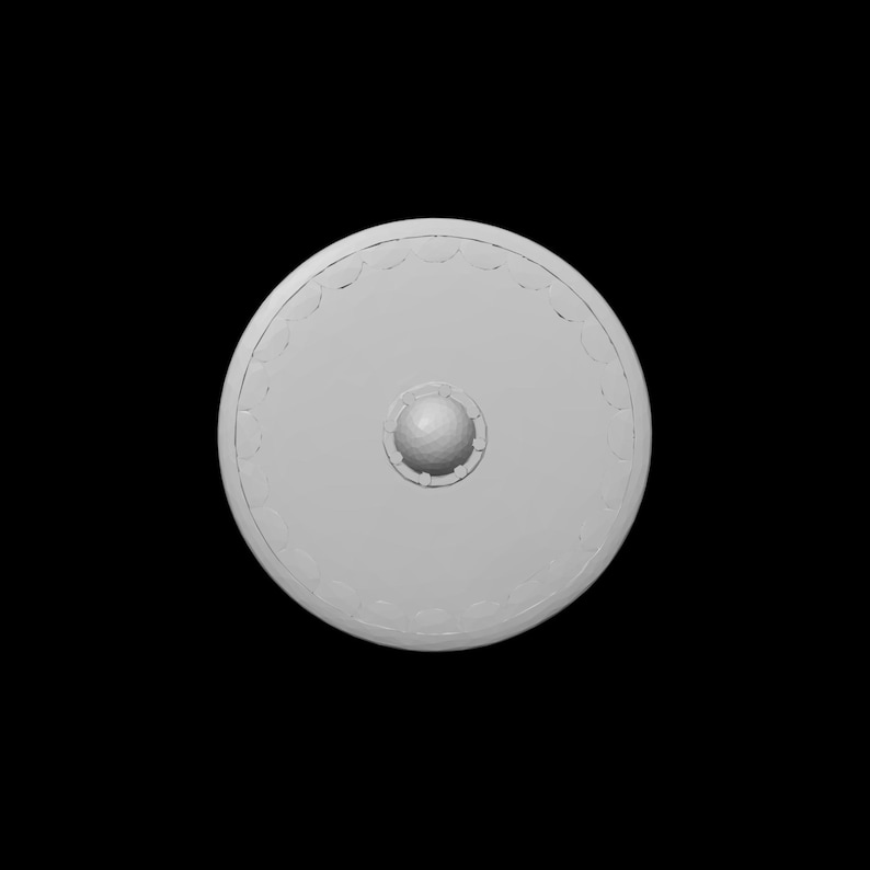 May include: A light gray, circular shield with a central, raised boss and a decorative border. The shield is set against a black background, highlighting its shape and design. The boss appears to be approximately 3 inches in diameter.