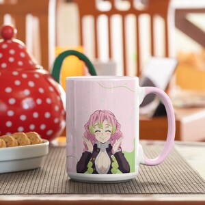 May include: A pink and white ceramic mug with a pink handle. The mug features a cartoon image of a pink-haired anime character with green eyes and a pink and green outfit. The character is smiling and has her hands raised in a gesture of excitement.