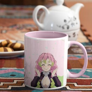 May include: A pink and white ceramic mug with a pink handle. The mug features a colorful anime character with pink hair and a green and black outfit. The background is pink with white dots.