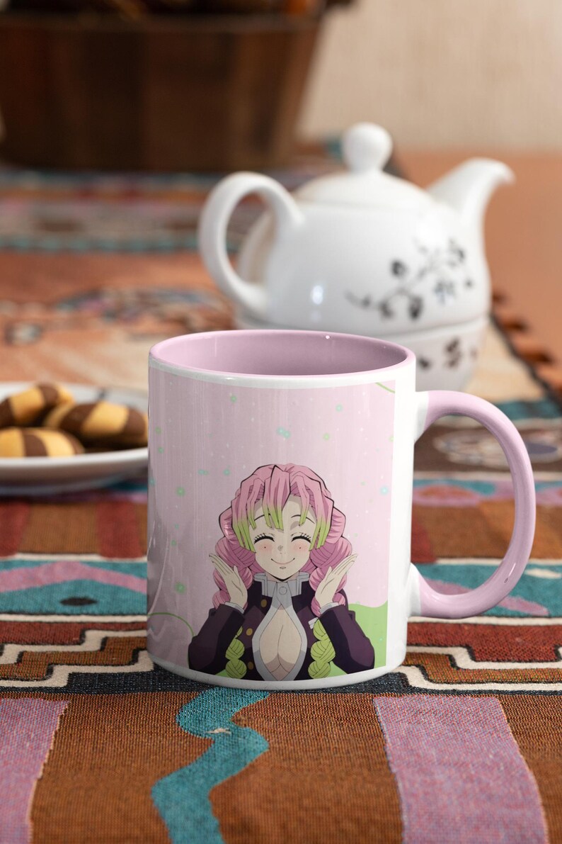 May include: A pink and white ceramic mug with a pink handle. The mug features a colorful anime character with pink hair and a green and black outfit. The background is pink with white dots.