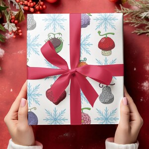 May include: A wrapped gift with a white patterned paper featuring colorful cartoon fruit and blue snowflakes. The gift is tied with a bright red ribbon and bow. The background is a festive red with holiday decorations.