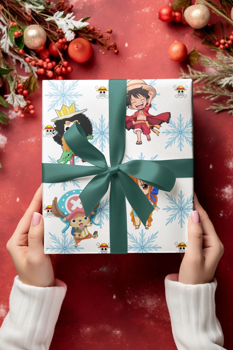 Pu&ograve; includere: Un regalo confezionato con un nastro e un fiocco verdi, con personaggi della serie anime One Piece. La carta da regalo &egrave; bianca con fiocchi di neve blu e illustrazioni di personaggi. Il regalo &egrave; tenuto su uno sfondo rosso con decorazioni festive.
