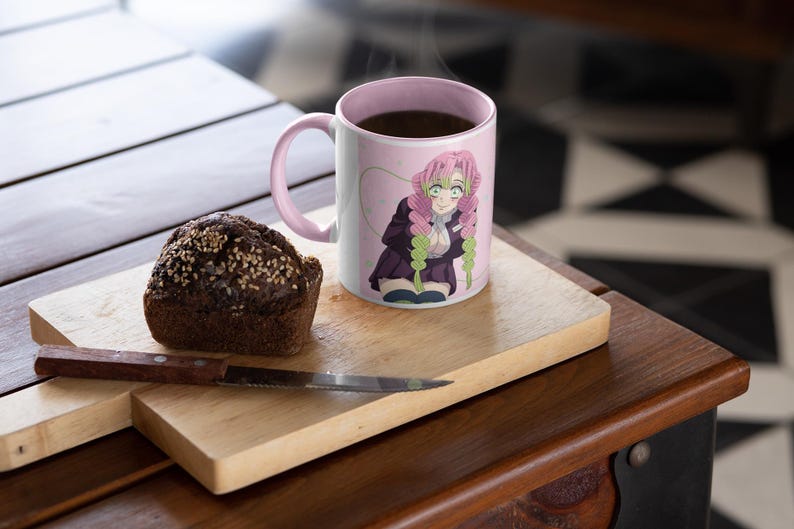 May include: A pink ceramic mug with a handle features a colorful anime character with pink hair and a green and purple outfit. The mug is filled with coffee and steam is rising from the top. A brown muffin is on a wooden cutting board next to the mug.