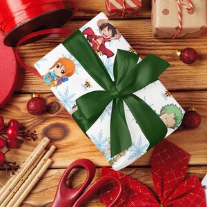 Pu&ograve; includere: Un regalo avvolto con un fiocco verde, con personaggi anime e fiocchi di neve, su una superficie di legno. Nastro rosso, ornamenti e un bastoncino di zucchero suggeriscono un tema festivo. La scena &egrave; festosa e colorata.