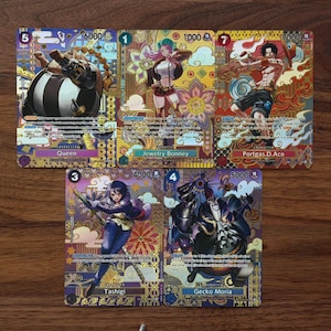 May include: Five colourful trading cards featuring anime characters. The cards show illustrations of characters named Queen, Jewelry Bonney, Portgas D. Ace, Tashigi, and Gecko Moria. Each card has a different point value.