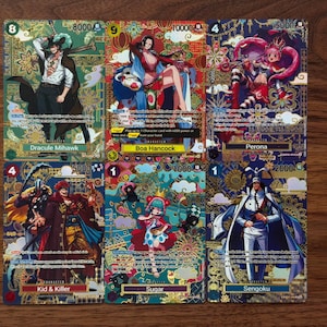 May include: Six collectible trading cards featuring characters from a popular anime series. Each card has a unique design with vibrant colours, gold accents, and character names. The cards are displayed on a wooden surface.