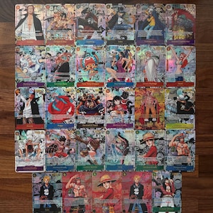 May include: A collection of holographic trading cards featuring various characters from the anime series One Piece. The cards have colorful illustrations and character names, with a wooden surface in the background.