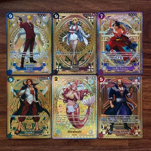 May include: Six collectible trading cards with gold and blue borders, featuring anime characters. The cards display illustrations of Sanji, Stussy, Luffy-Tarou, Shanks, Shirahoshi, and Silvers Rayleigh. Each card has character names and numerical values.