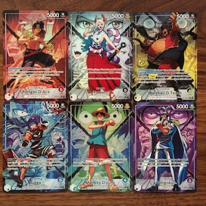Può includere: Sei carte collezionabili con personaggi anime colorati. Ogni carta mostra il nome di un personaggio e un valore di 5000. I personaggi includono Portgas D. Ace, Yamato, Marshall D. Teach, Buggy, Monkey D. Luffy e Sengoku.
