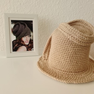 Peut inclure: Un chapeau en crochet beige à large bord. Le chapeau est plié d'un côté, créant une forme unique.