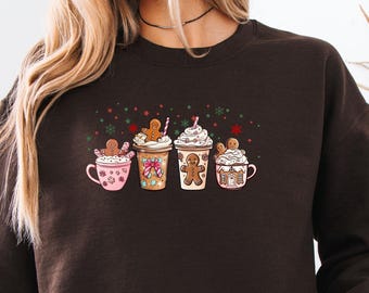 May include: Dark chocolate-colored sweatshirt featuring a festive graphic of four holiday-themed coffee cups with gingerbread men and whipped cream. The cups are decorated with bows, sprinkles, and holiday accents. The text "DARK CHOCOLATE" is printed on the bottom right.