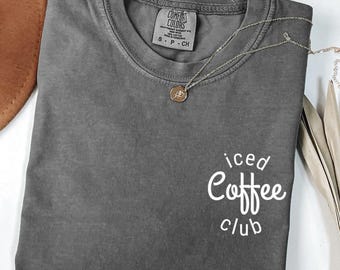 May include: A gray Comfort Colors t-shirt with the words "iced Coffee club" in white script. A gold necklace with a pendant rests on the shirt. The word "pepper" is visible in the bottom left corner.