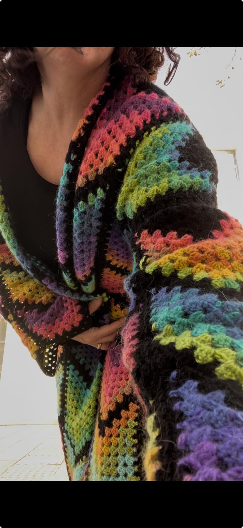 May include: A colorful, handmade crochet cardigan in a rainbow of hues, including pink, orange, yellow, green, blue, and purple. The cardigan has a black border and a textured, open weave design. A cozy and vibrant piece of wearable art.
