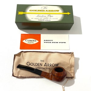 Pode incluir: Um cachimbo de madeira marrom com um bocal preto e uma bolsa de couro marrom. O cachimbo é etiquetado como "The Golden Arrow London Pipe".