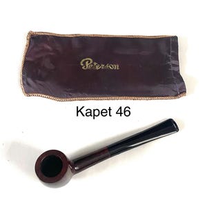 May include: A Peterson Kapet 46 pipe with a dark brown bowl and stem, and a black mouthpiece. The pipe is accompanied by a dark purple pouch with gold text that reads "Peterson". The text "Kapet 46" is below the pouch.