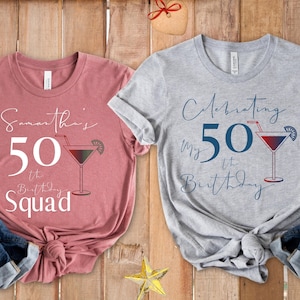 May include: Two t-shirts with birthday-themed designs. One is dusty rose with "Samantha's 50th Birthday Squad" text and a cocktail graphic. The other is gray with "Celebrating my 50th Birthday" text and a cocktail graphic.