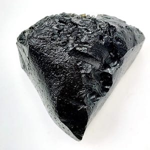 May include: A large, irregularly shaped, black obsidian stone with a glossy, textured surface. The stone has sharp edges and a rough, natural appearance, set against a white background.