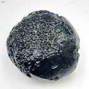 May include: A dark, rounded stone with a textured, bubbly surface. The stone is primarily black with areas of lighter, web-like patterns. The overall shape is irregular, with a smooth, glossy appearance in some areas.