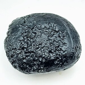 May include: A dark, irregularly shaped, black tektite with a rough, textured surface. The natural glass formation has a glossy sheen and a unique, organic appearance. The tektite is a solid, rounded shape, likely a meteorite.